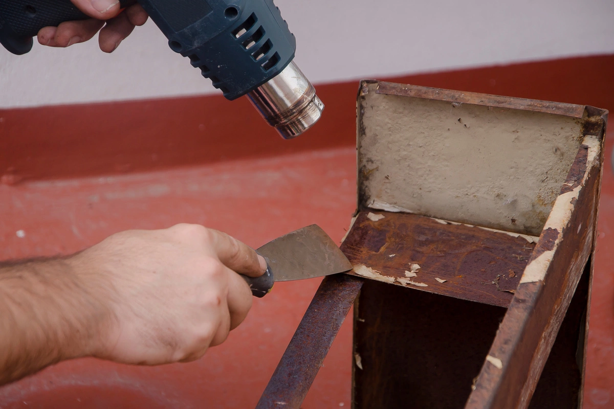 homme décapant de la peinture sur un mobilier avec une spatule et un pistolet à chaleur